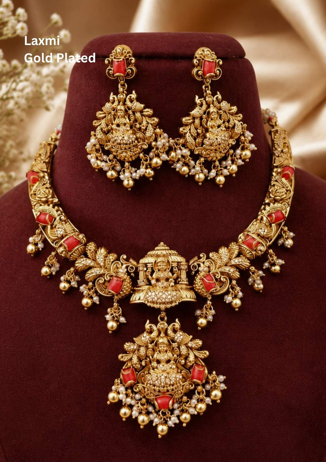 A grand antique gold plated temple haram jewelry set featuring a multi-segment link necklace carved with small seated deities and inset with smooth red coral stones. The center showcases a miniature temple mandapam structure over a large chandelier pendant depicting Goddess Lakshmi, fringed with tiny white hanging pearls. It comes with matching heavy statement drop earrings.