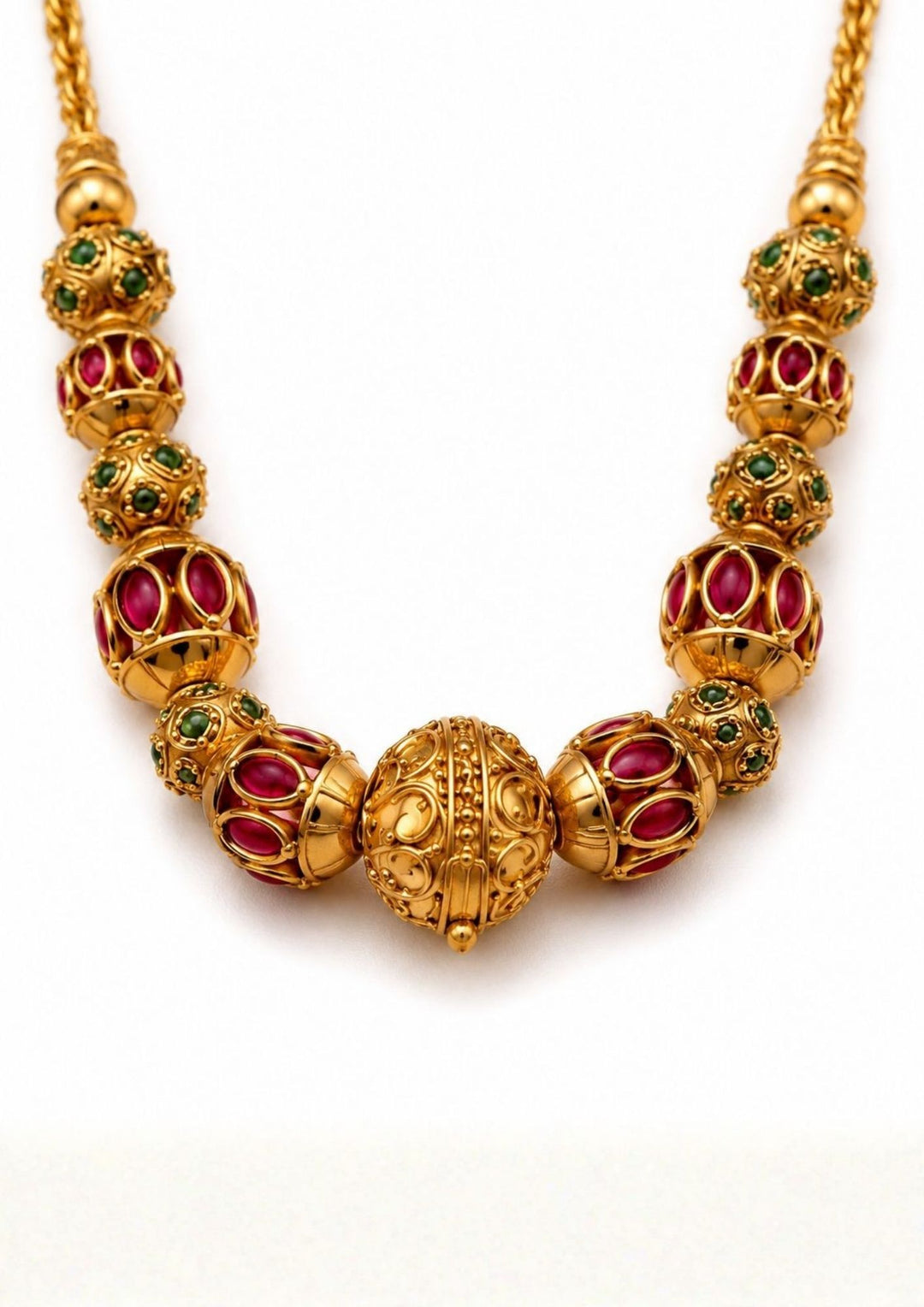 Close up view of Gold plated long chain haraam necklace featuring elegant textured golden spheres alternating with small spacer rings inset with red ruby and green emerald stone accents. This lightweight chain is crafted with a detailed twisted rope style chain extension held in hand to provide a classy and premium appearance suitable for daily wear, office wear, casual outings, family gatherings, festivals, parties and traditional occasions with skin friendly quality, anti fade polish, comfortable fitting