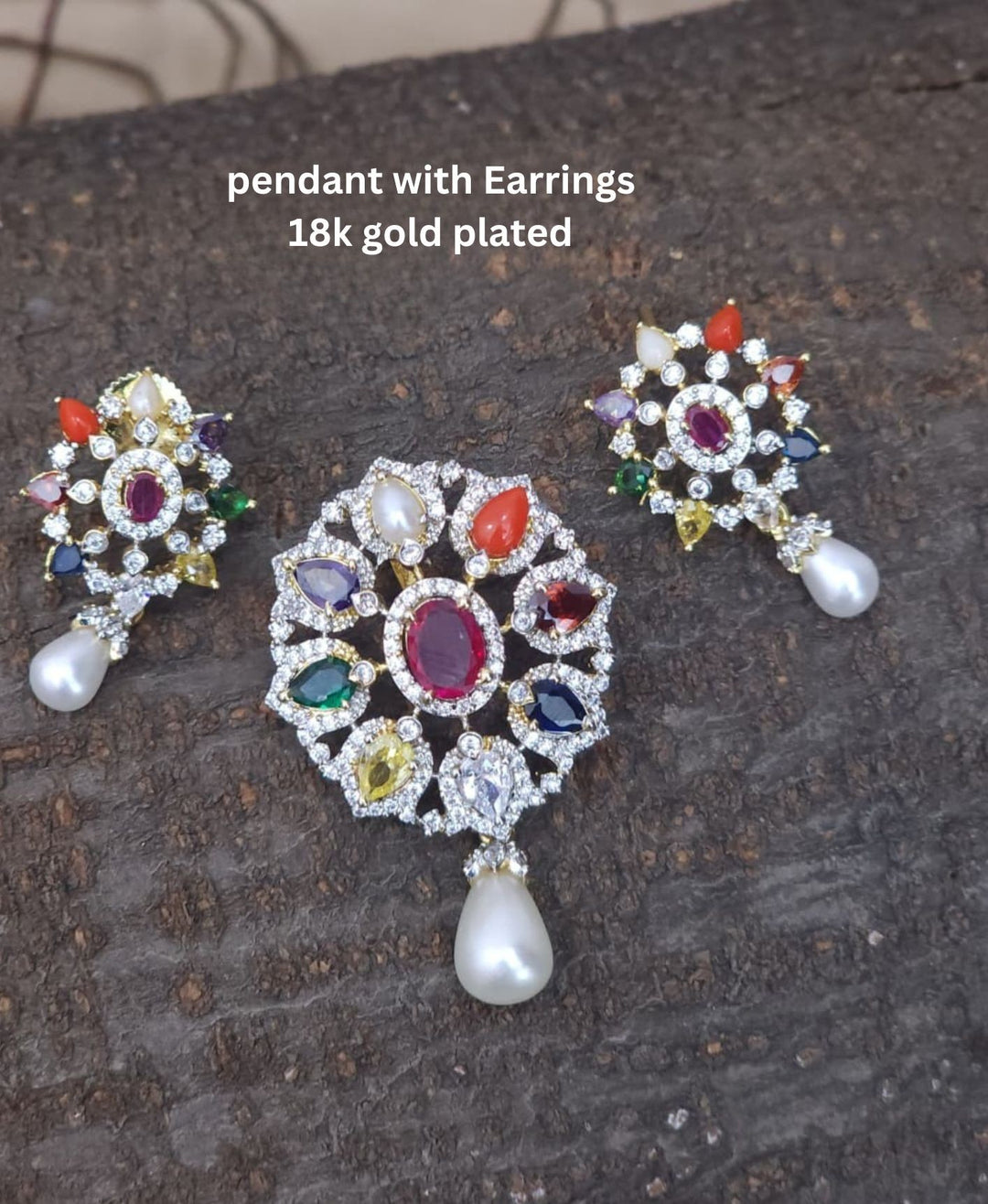 Gold-plated pendant necklace and matching stud earrings displayed on a black velvet jewelry bust. The necklace features a detailed floral pendant with red, green, and blue stones, while the matching earrings are shown above the bust.