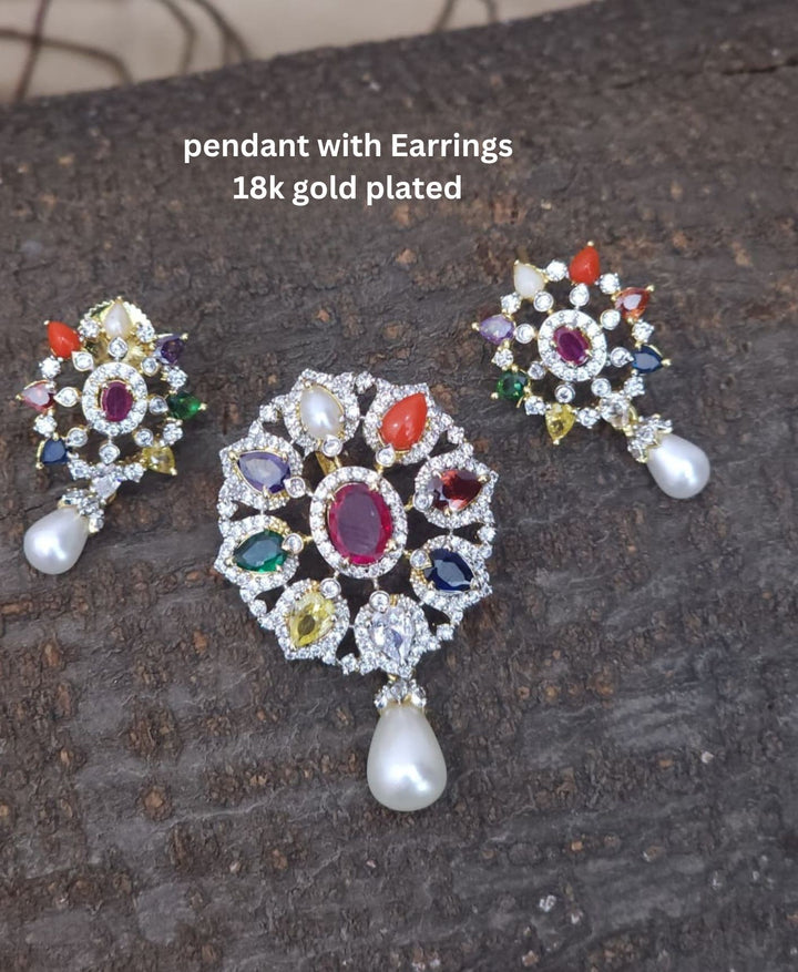 Gold-plated pendant necklace and matching stud earrings displayed on a black velvet jewelry bust. The necklace features a detailed floral pendant with red, green, and blue stones, while the matching earrings are shown above the bust.