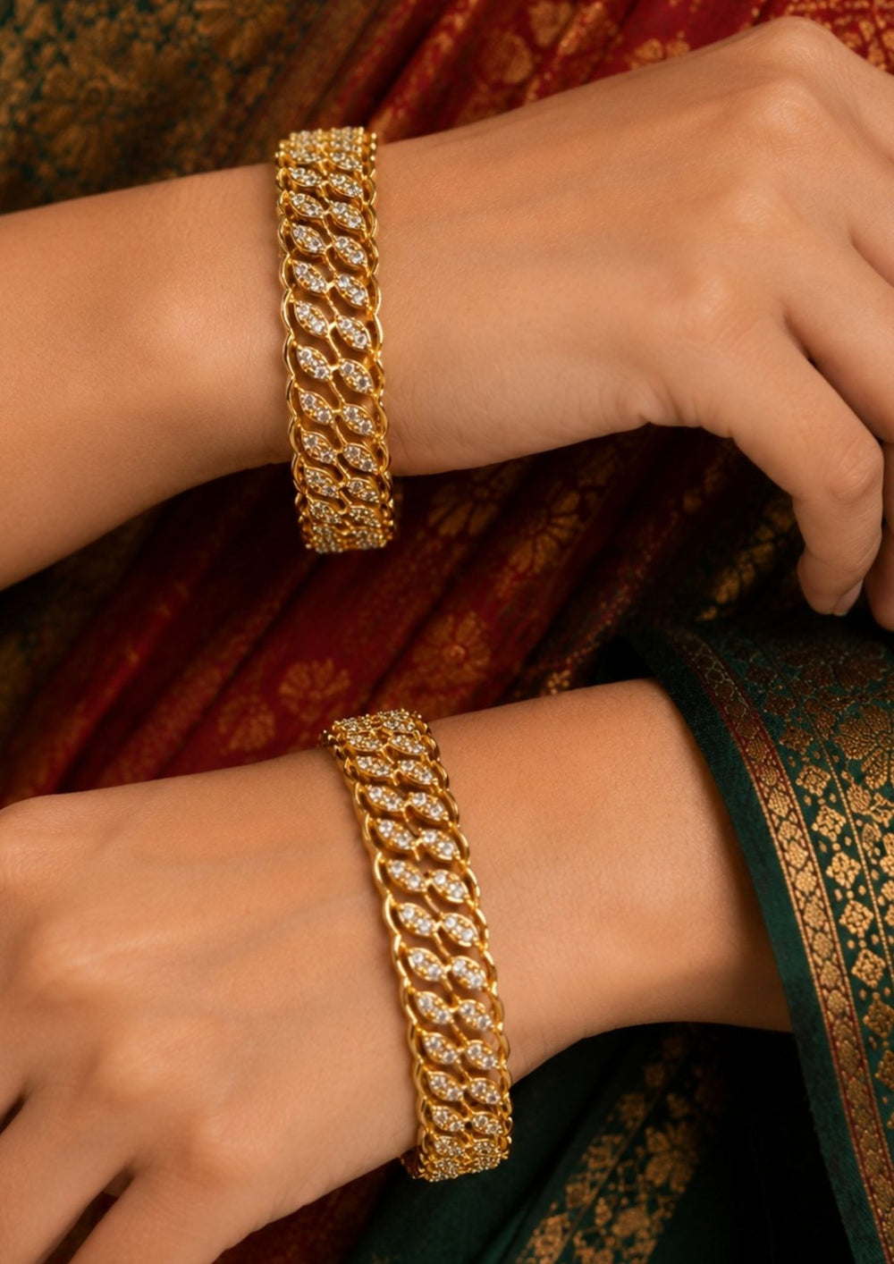 Closeup of women hands wearing A sophisticated pair of sleek gold-plated bangles embellished with shimmering white Zircon diamonds. The design features a continuous, intertwining wave or leaf-like pattern intricately handset with sparkling crystals for a diamond-like brilliance. ideal for parties and special occasions.