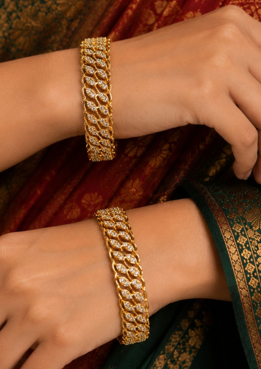 Closeup of women hands wearing A sophisticated pair of sleek gold-plated bangles embellished with shimmering white Zircon diamonds. The design features a continuous, intertwining wave or leaf-like pattern intricately handset with sparkling crystals for a diamond-like brilliance. ideal for parties and special occasions.