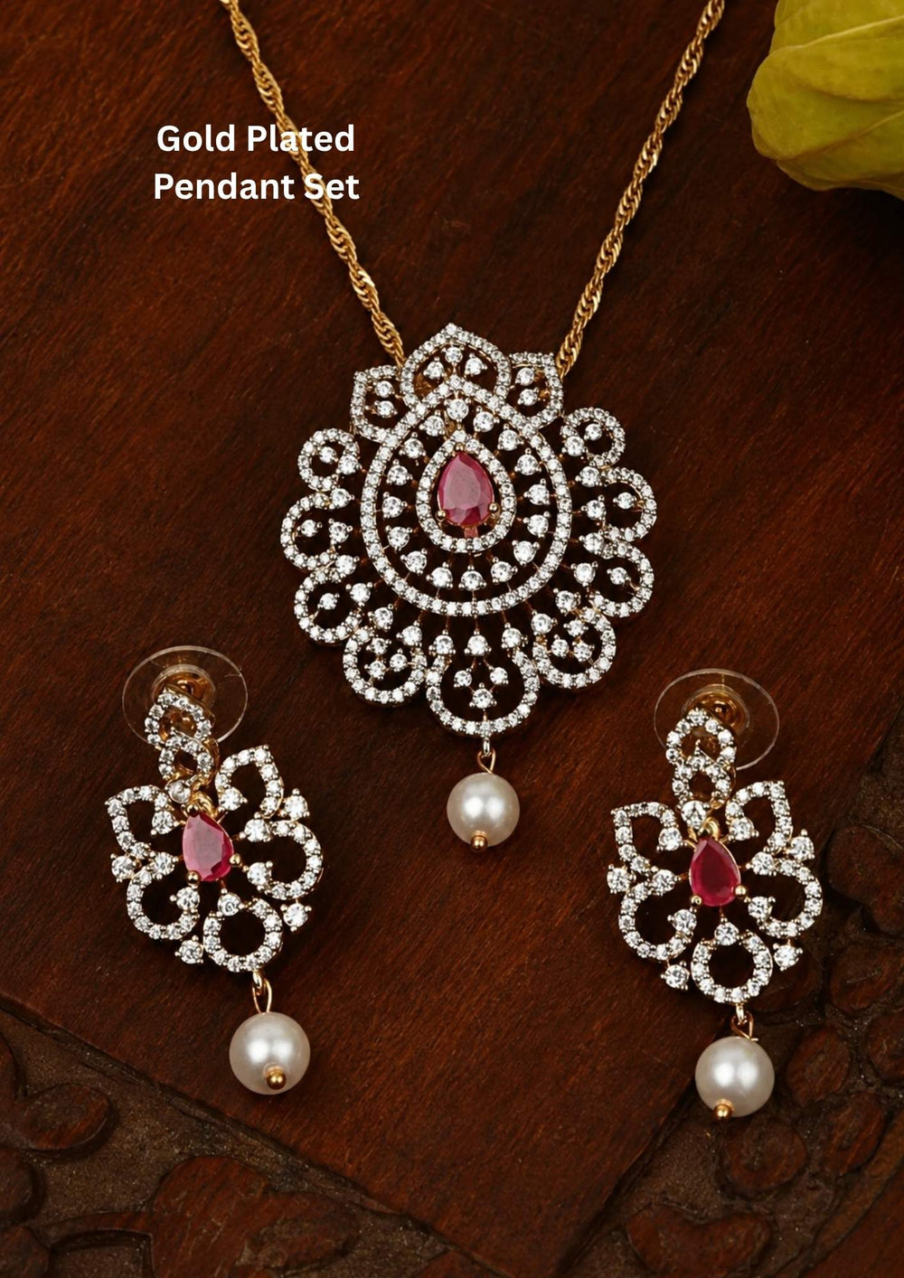 Elegant zircon diamond gold plated pendant set featuring a floral-inspired pendant designed with sparkling white zircon stones arranged in circular patterns. The centerpiece showcases a pear-shaped emerald red stone surrounded by dazzling zircon stones, finished with a delicate pearl drop. The matching earrings mirror the same floral design with green stone and pearl danglers, Perfect for weddings, festivals, office wear, functions and its anti fade color