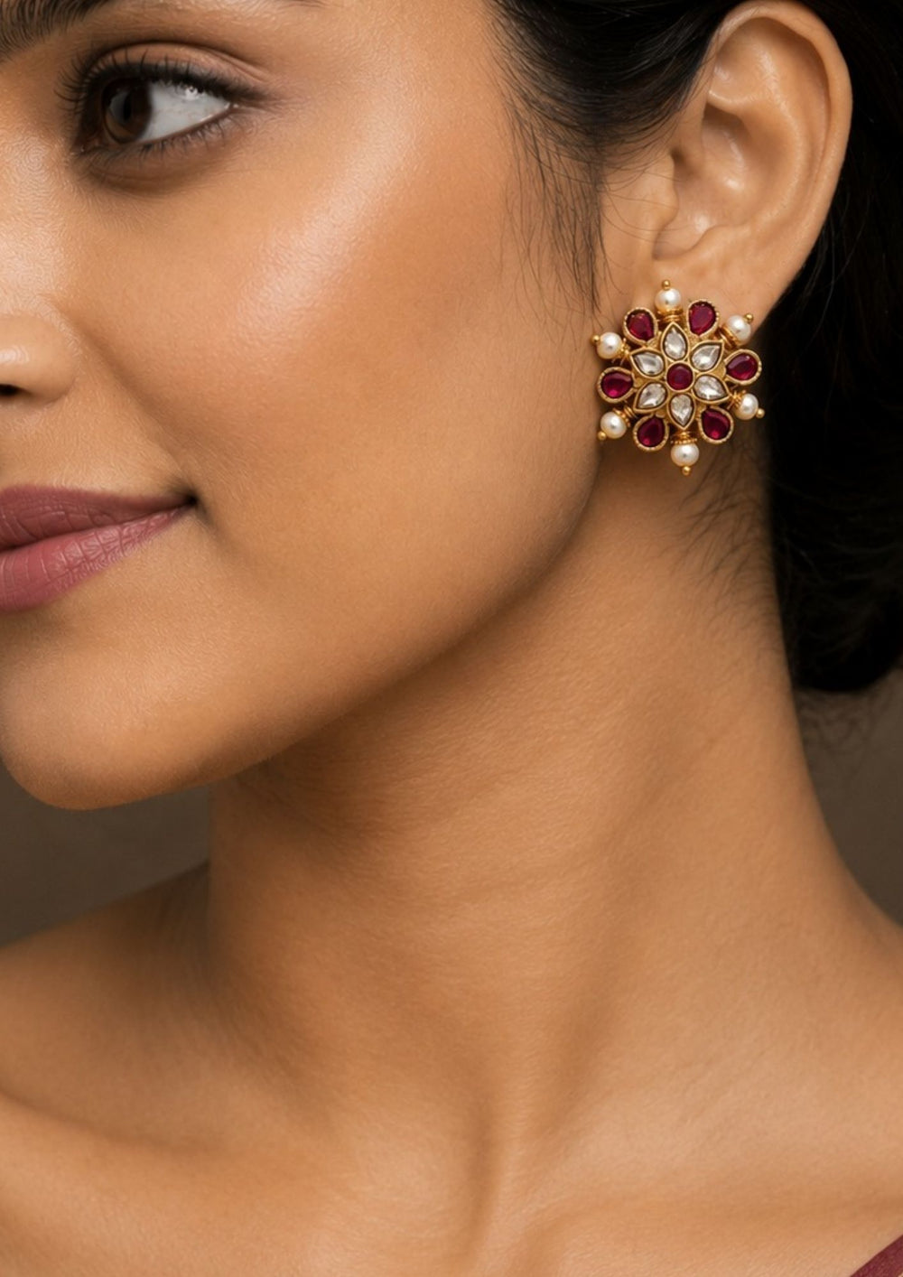 A close-up of a south indian women ear wearing Gold-plated Jadau kundan studs with push back come with pink gemstone and looks very elegant and  comes with much detailed look and can use for daily ware, functional ware, festive ware and perfect for giffting 