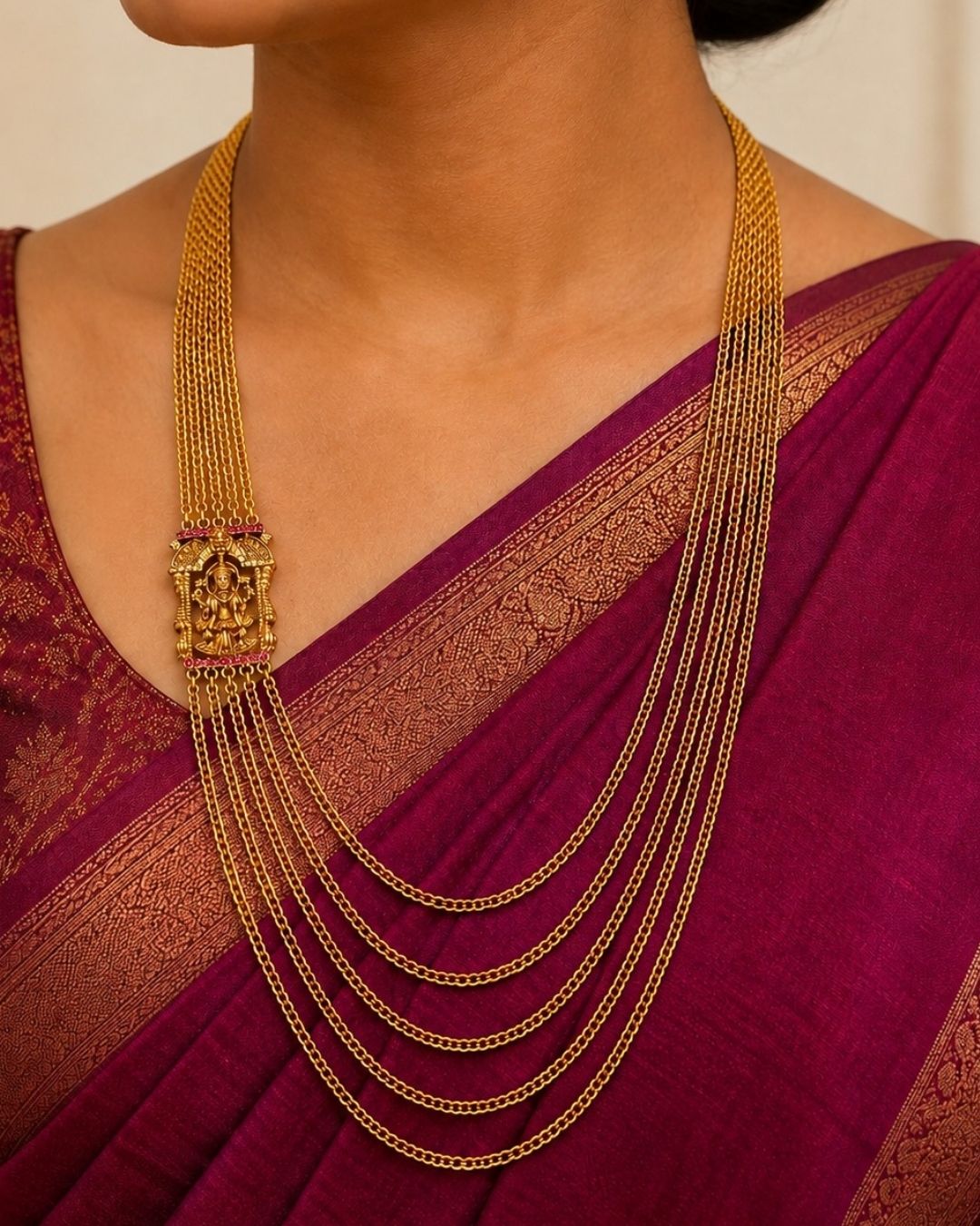 Beautiful traditional gold plated necklace featuring multiple layered chains and a detailed goddess pendant with red and green accents. Perfect for festive occasions, traditional outfits, weddings, parties, and gifting.
