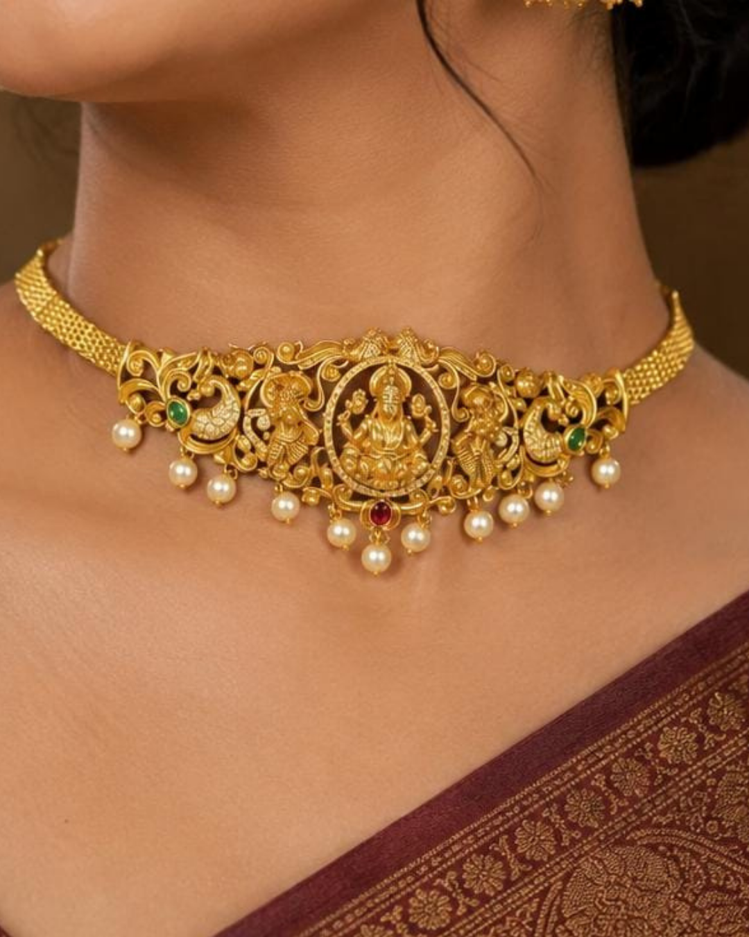 Premium gold plated 2-in-1 choker and bajuband featuring Goddess Lakshmi surrounded by intricate peacock and floral-inspired detailing, accented with green and pink stones and elegant pearl drops. Perfect for weddings, festive occasions, traditional wear, dance performances, parties and gifting.