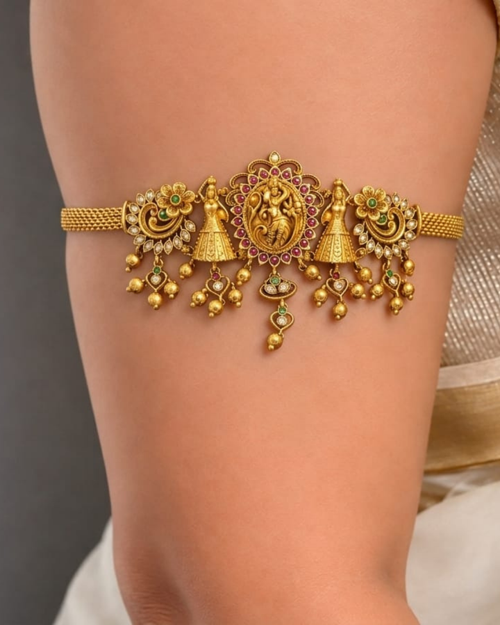 Beautiful gold plated 2-in-1 choker and bajuband set featuring Goddess Lakshmi, peacock and floral motifs embellished with green and pink stones and delicate hanging gold beads. Perfect for weddings, festive occasions, traditional wear, Bharatanatyam styling, parties and gifting.
