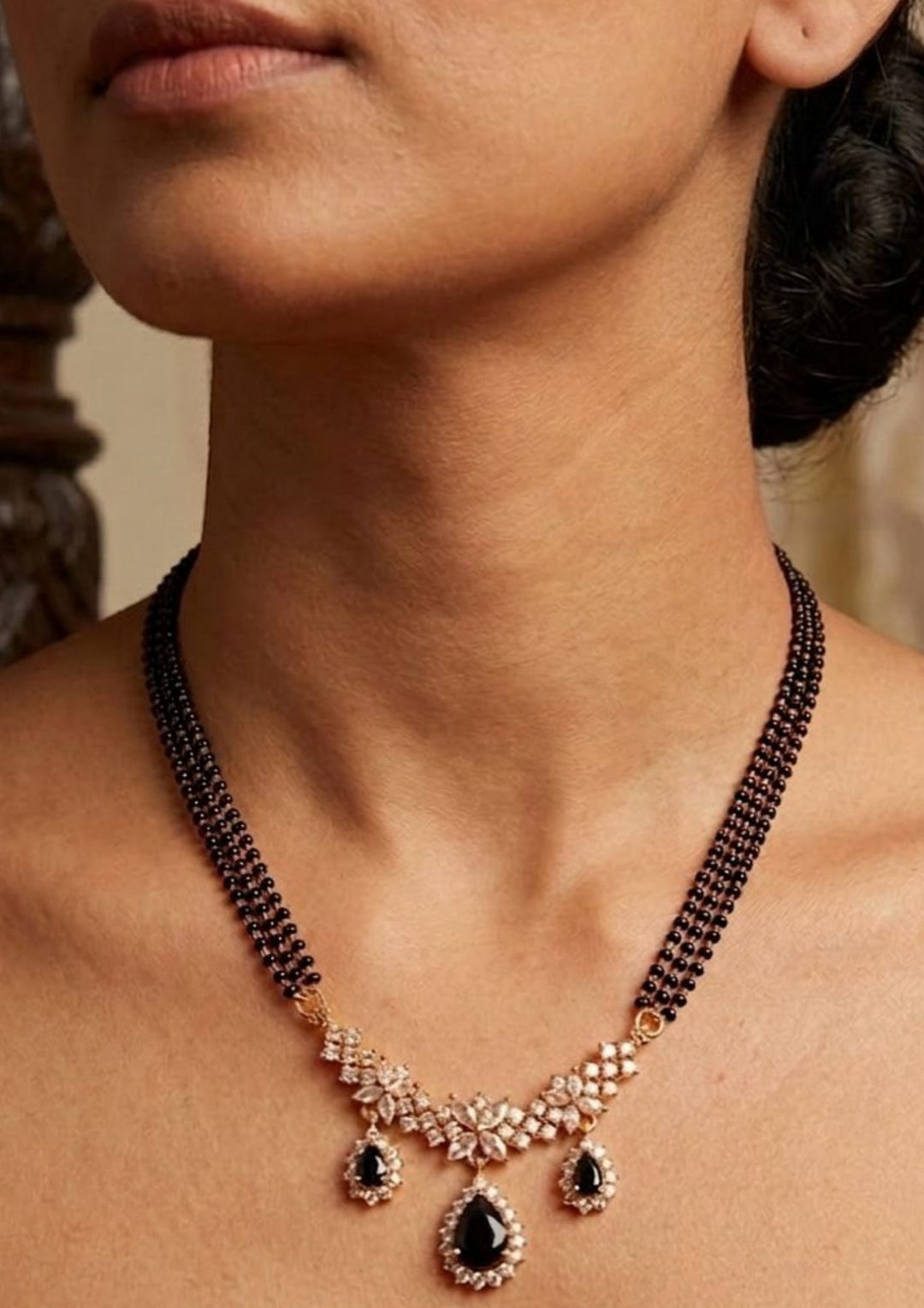 Close-up of South indian women wearing an 18K Gold Plated mangalsutra necklace set highlighting the half moon pendant design covered in white zircon diamonds. The three-layered black bead chain pattern offers a lightweight, sweat-proof, and anti-fade quality, making it an elegant, comfortable jewelry choice for daily wear, festivals, and special events.