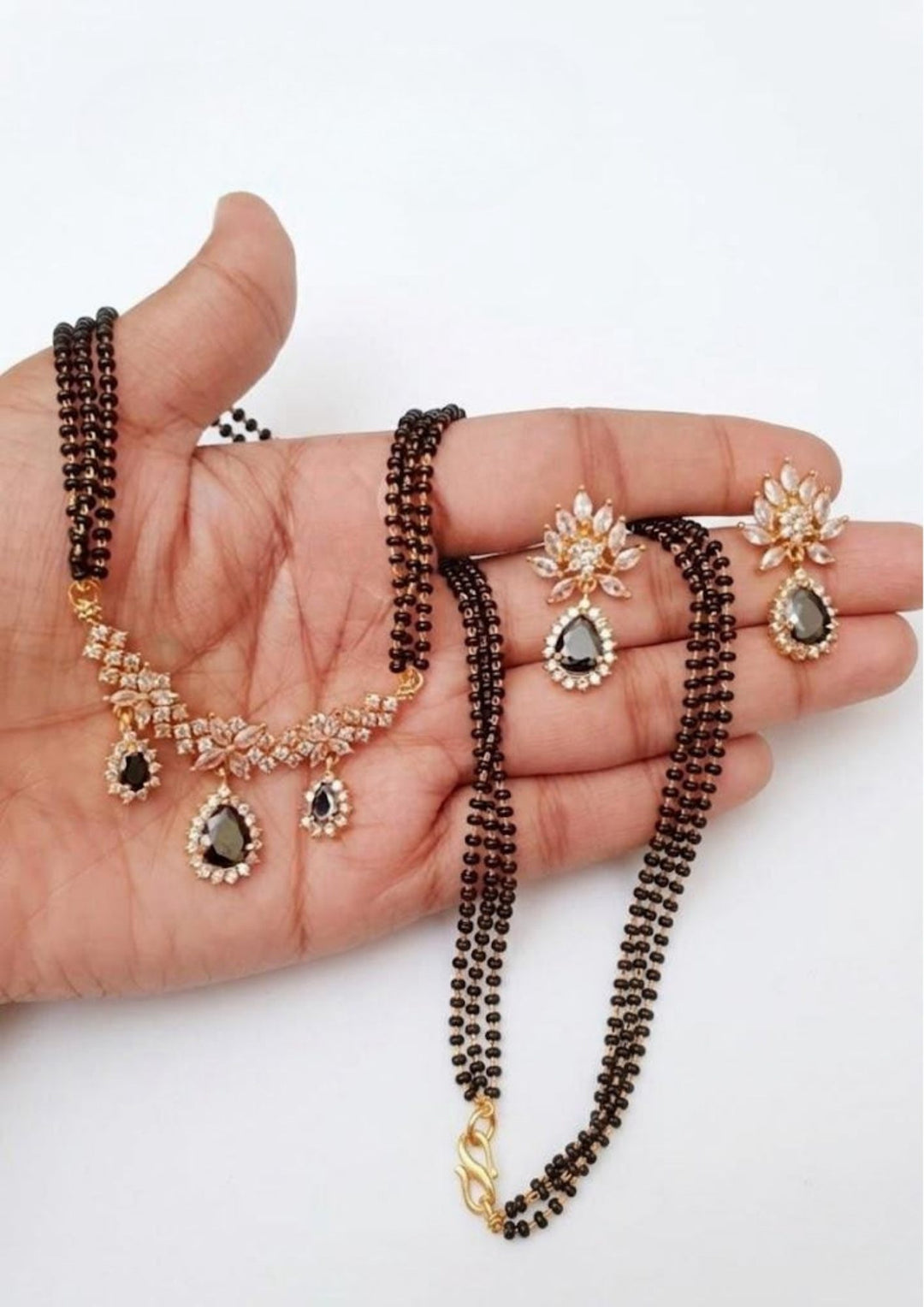 Hand holding a necklace and earrings set on a white background and comes with flower design and with emeralds stones  and can see pic in white background very clearly 