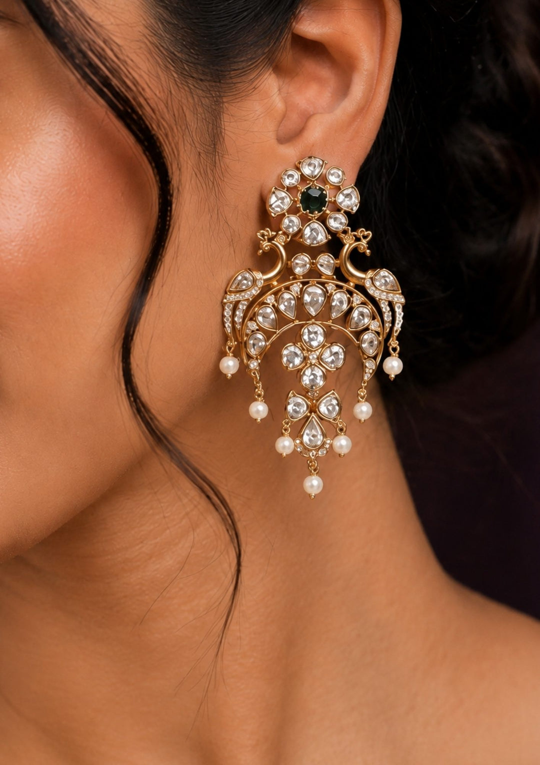 Close-up of a person wearing an ornate gold earring with pearls and a green gemstone.